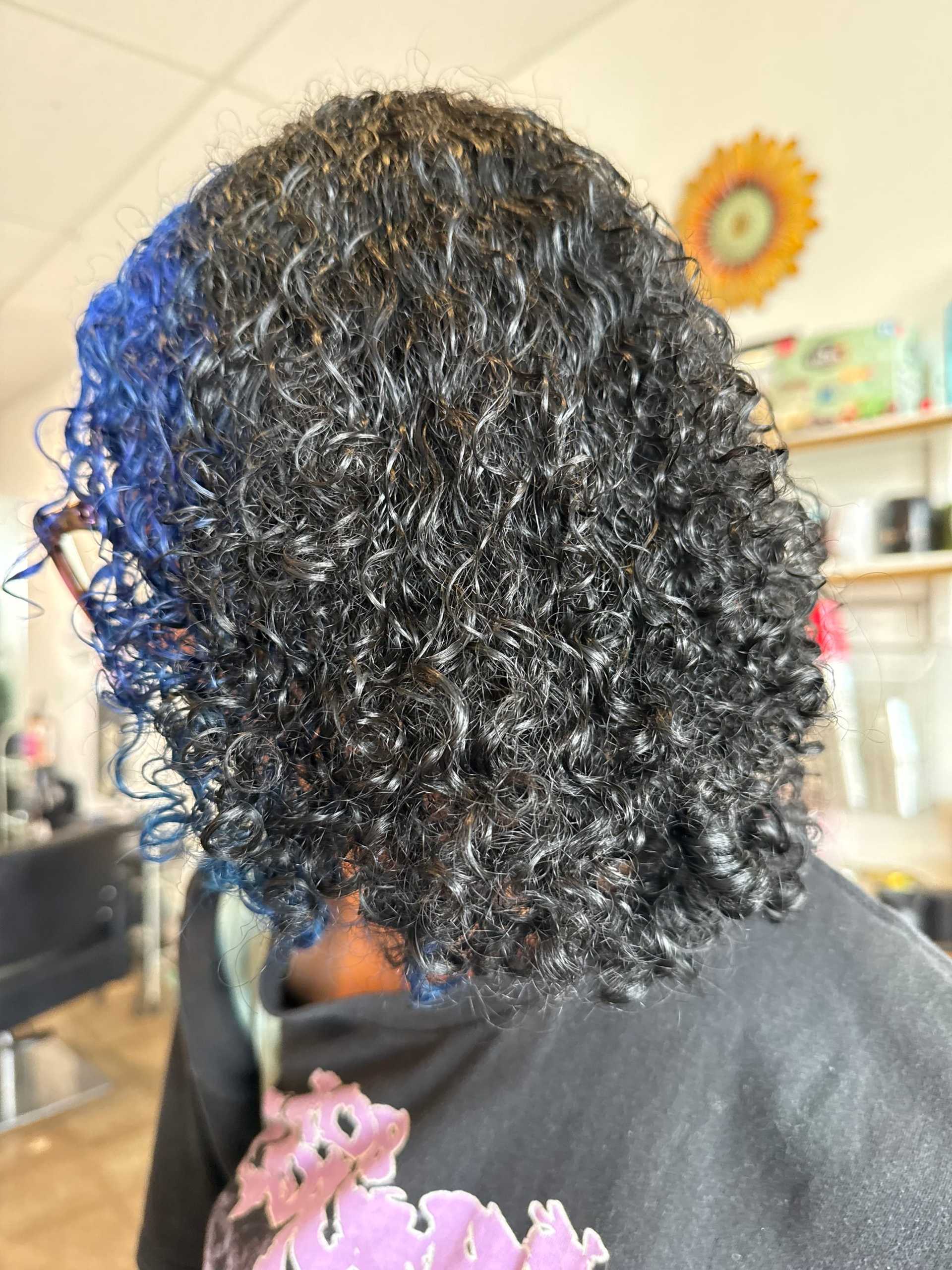 Curly hair styled in salon with colorful wall art in the background.