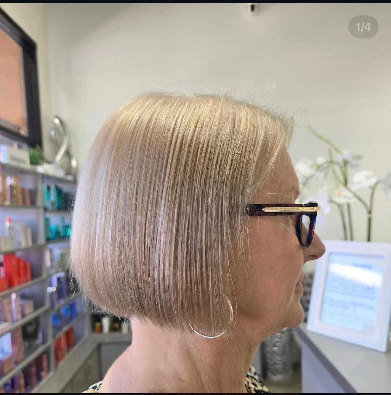 Short bob haircut on a woman with glasses. Shelves with hair products in the background.