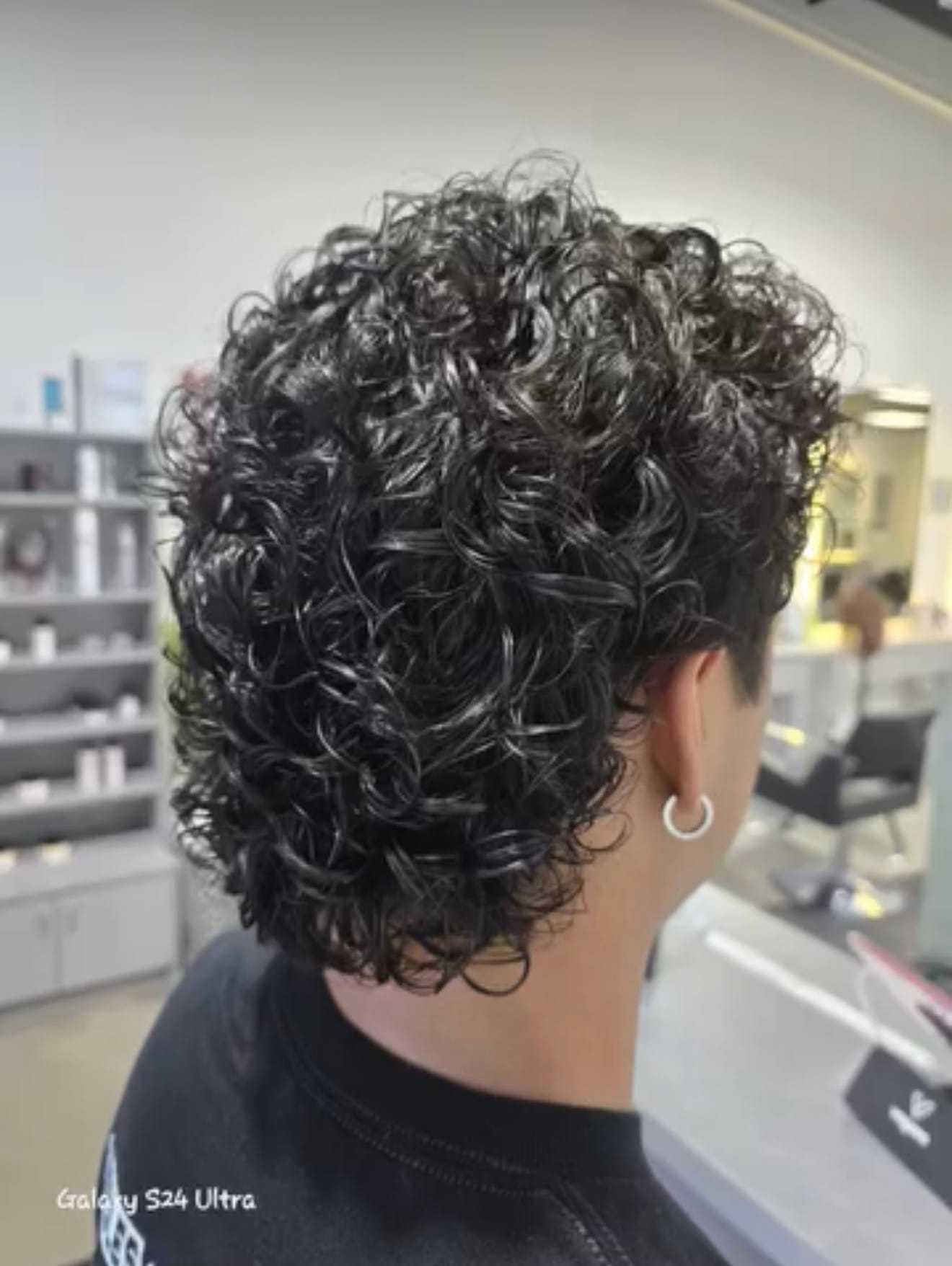 Curly-haired person with an earring, standing in a modern, brightly lit salon.