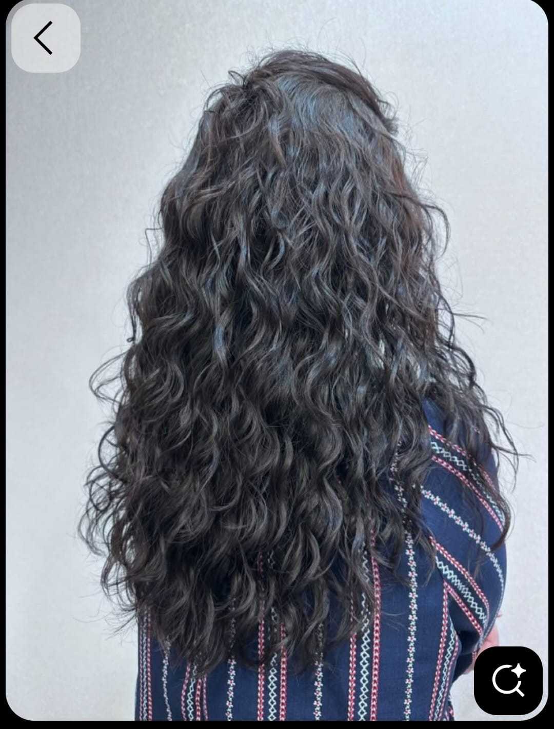 Curly brown hair cascading down a person's back, wearing a patterned shirt.