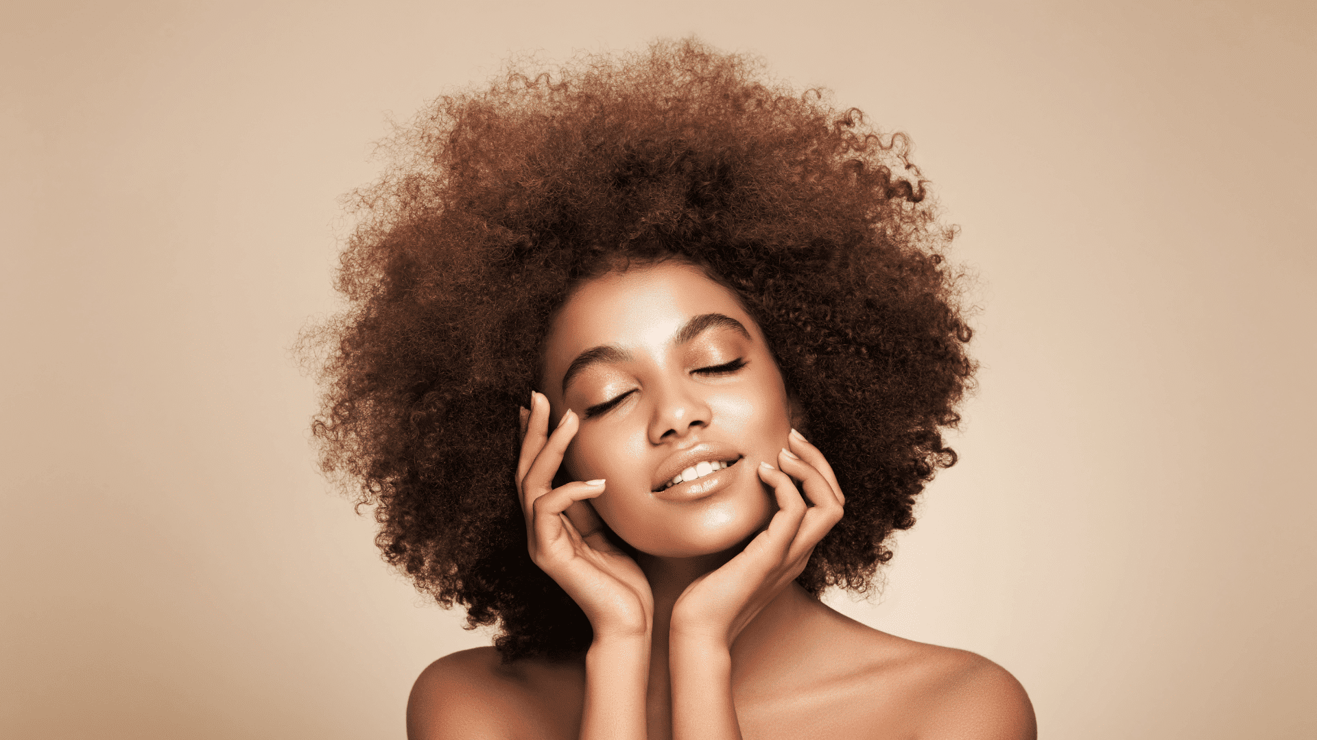 Woman with curly hair and closed eyes smiling peacefully against a beige background.