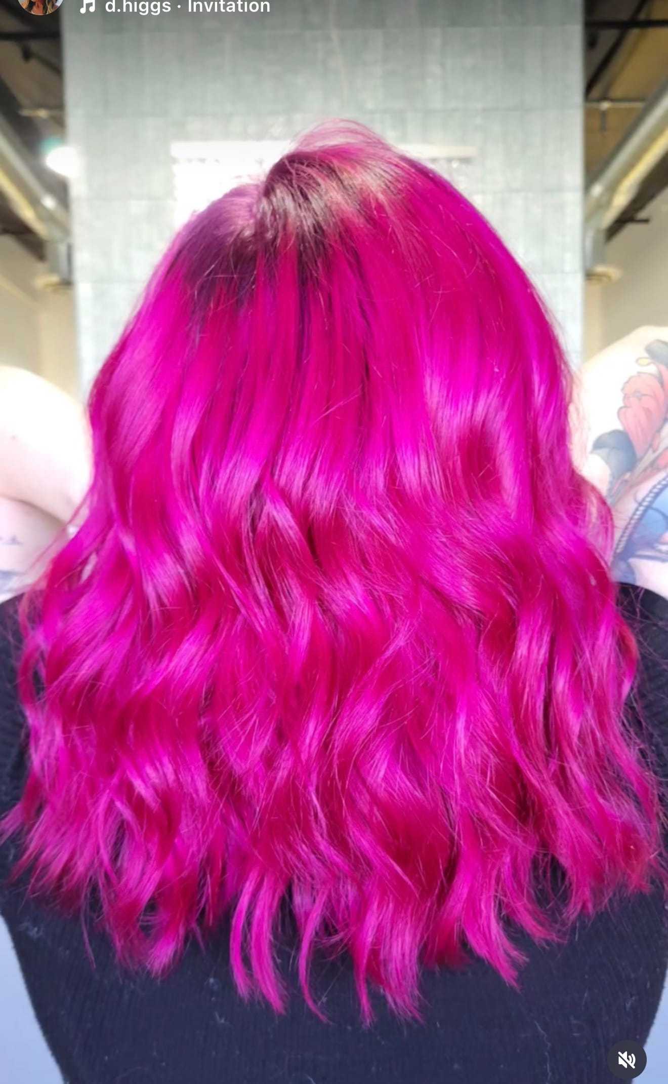 Bright pink wavy hair with tattooed arms visible in the background.